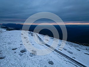 snow covered mountains at sunset with a winding road in the foreground aerial view
