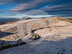 snow covered mountains at sunset with a winding road in the foreground aerial view