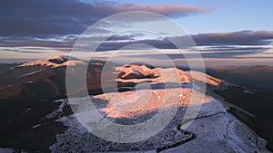 snow covered mountains at sunset with a winding road in the foreground aerial view