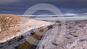 snow covered mountains at sunset with a winding road in the foreground aerial view