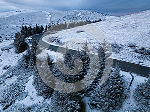 snow covered mountains at sunset with a winding road in the foreground aerial view