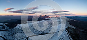 snow covered mountains at sunset with a winding road in the foreground aerial view