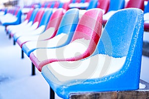 Snow-covered multi-colored seats in the stadium in winter. Snowfall interferes with sports. Uncleaned stadium. ecological