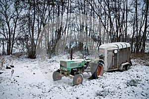 Snow-covered old rusted tractor with a livestock transport trailer