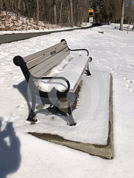 snow covered park bench beside walkway, at Dean Park Shrewsbury MA