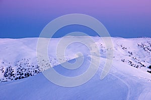 Snow-covered peaks of mountains in the rays of the sunrise in the winter frosty morning.