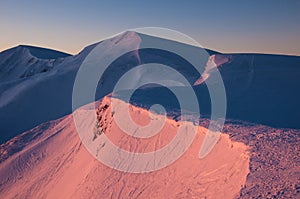 Snow-covered peaks of mountains in the rays of the sunrise in the winter frosty morning.