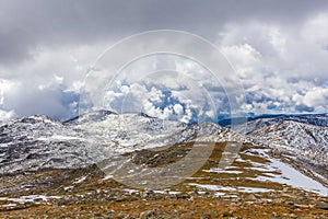 Snow covered peaks and yellow grass under clouds. Australian Alp