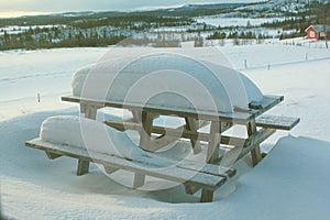 Snow covered picnic table in the garden of a mountain village house in the morning sun. The concept of a family holiday in the