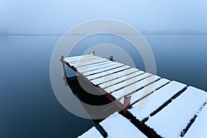 Snow-covered pier on the lake on a foggy day