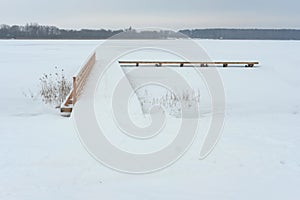 Snow covered pier over a frozen lake - winter landscape