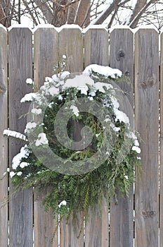 Snow covered pine juniper wreath wood fence gate