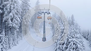 The snow-covered piste for skiers and snowboarders is laid out among snow-covered spruce trees. Nearby, a chairlift runs on metal