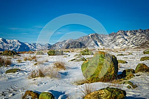 Snow-covered plain among the mountains against blue sky on a sunny winter day. Vast mountain ranges on the horizon