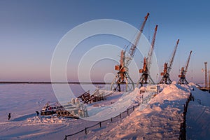 The snow-covered port cranes and snow piles on the frozen Pechora river bank at Naryan-Ma. photo