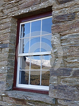 Snow covered range reflected in historic stone cottage window, New Zealand