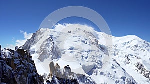 Snow covered rocky peaks of the alpine mountains. Mont Blanc mountain in a cloud against a blue sky