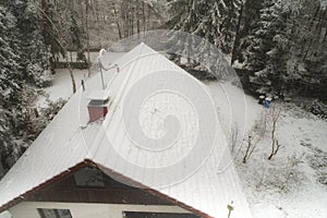 Snow-covered, roof, of a detached house in a forest with a snow-covered satellite antenna and pines at the edge