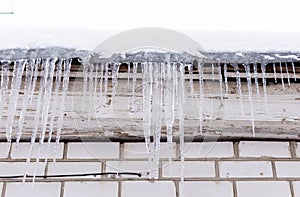 Snow-covered roof of a house with icicles on background of white brick wall