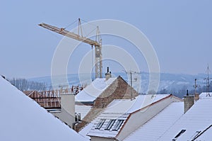 Snow-covered roofs with chimneys, antennas and tower crane.