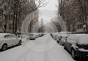 Snow-covered street with cars parked on both sides in the cold season, Bucharest, Romania.