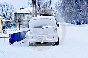 On a snow-covered street there is a car covered with snow