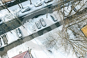 Snow-covered trees and cars on parking lot. winter season in city. aerial top view