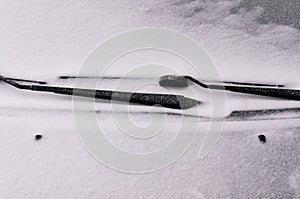 Snow covered windshield with wiper blades. Concept of driving in winter time with snow on road. Winter season