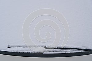 Snow covered windshield with wiper blades. Frozen snow on car in cold winter morning. Concept of driving in winter time