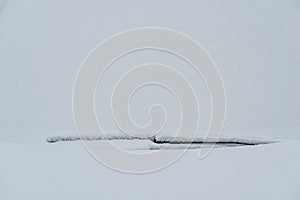 Snow covered windshield with wiper blades. Frozen snow on car in cold winter morning. Concept of driving in winter time