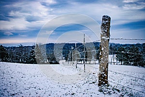 Snow covered winter field in the country with fence and trees landscape
