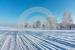 Snow covered winter field with trees and road going through to the horizon. Winter landscape.