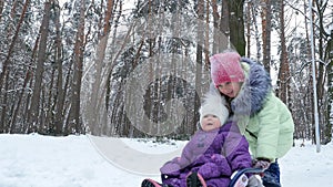 In the snow-covered winter forest, two girls, one year and seven years old, have fun sledding. the elder sister rolls