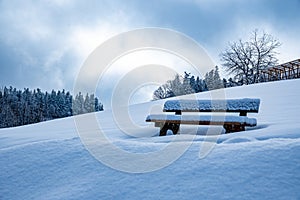 Snow-covered wooden bench in the idyllic winterlandscape in the mountains