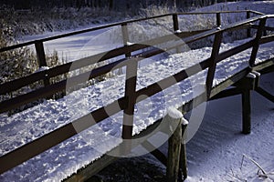 Snow-covered wooden bicycle and walking bridge with railing over a frozen ditch