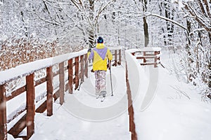 Snow covered wooden bridge in forest, skier, back to us