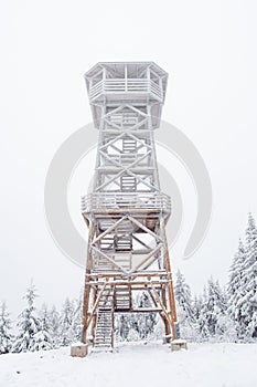 A snow-covered wooden lookout tower on top of the Czernica Mountain. Winter landscape in the Sudetes on a hiking trail