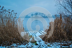 A snow-covered wooden platform in the reeds and a frozen misty lake