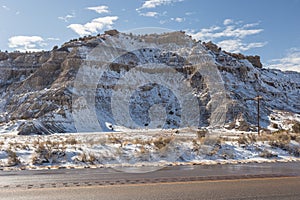 Snow covering interesting rock formations desert along empty highway on clear blue day