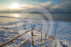 Snow Curonian Spit dunes in January winter sunny day. Blue sky and sea, no people on the beach, wooden stairway, calm