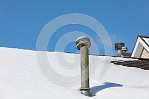 Snow drift on roof around furnace exhaust flue after winter storm.