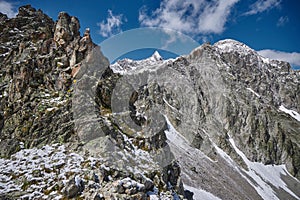 Snow dusted mountain peaks tower against a bright blue sky, with rocky outcrops and steep inclines