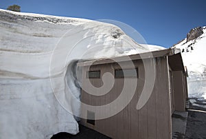 Snow envelops the top of an outhouse