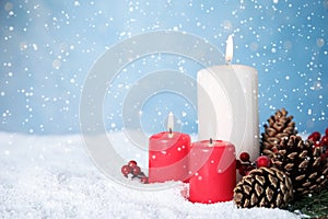 Snow falling on burning candles and pine cones against light blue background, space for text. Christmas eve