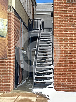 Snow falls on the sidewalks downtown and on the stairs by the red brick office buildings.