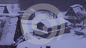 Snow falls on steep thatch roofs of Gokayama village in grey dawn