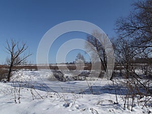 Snow on a frozen pond is covered by blue shadows