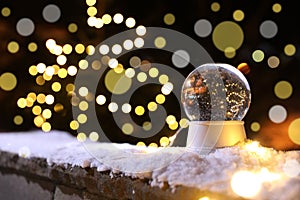 Snow globe and blurred Christmas lights on background. Winter decor