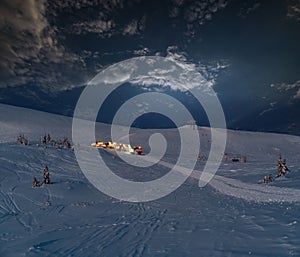 Snow groomers on night predawn excursion ride to winter mountain top with freeriders snowboarders.