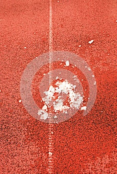 Snow on ground. White lines and texture of running racetrack, red racetrack, in outdoor stadium